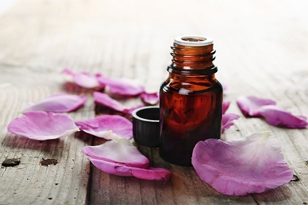 amber bottle and rose petals on wooden surface